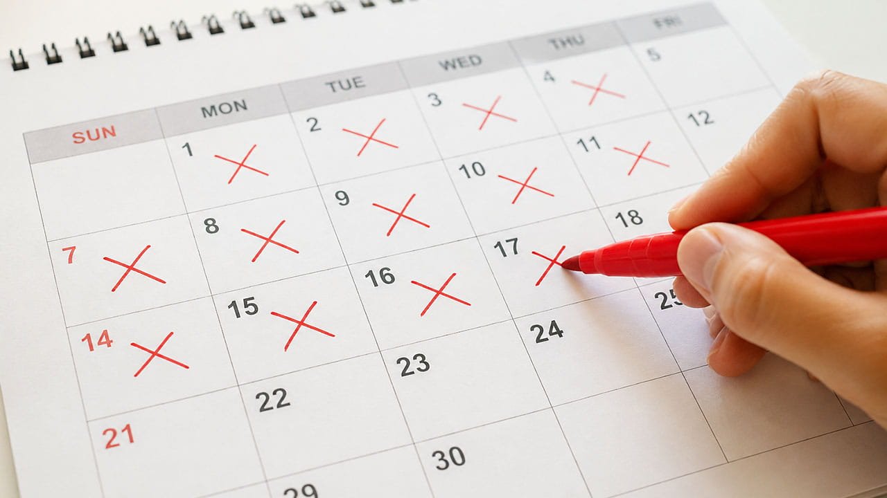 Mão marcando dias em um calendário com caneta vermelha, representando o acompanhamento do ciclo menstrual e sintomas como dor pélvica crônica e endometriose.