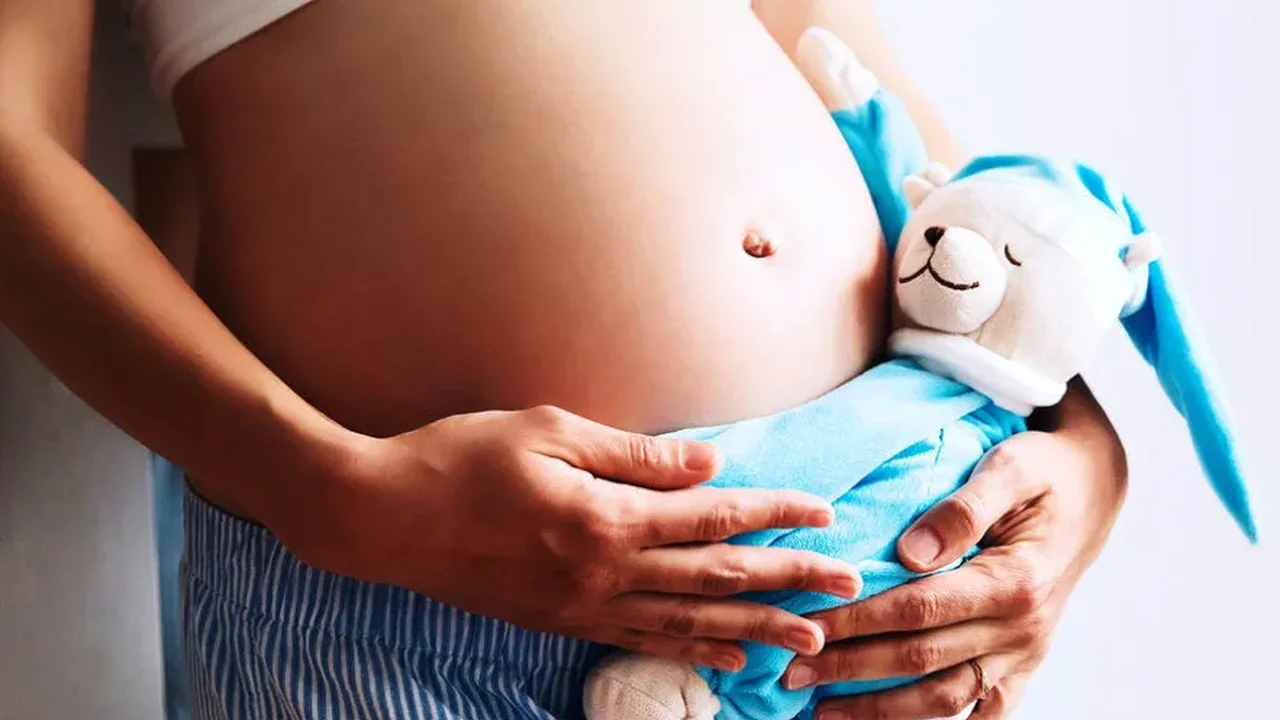 Gestante segurando uma peça de roupa de bebê diante da barriga.